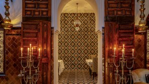 Un intérieur traditionnel avec des portes en bois richement décorées, un sol carrelé à motifs et des chandeliers.