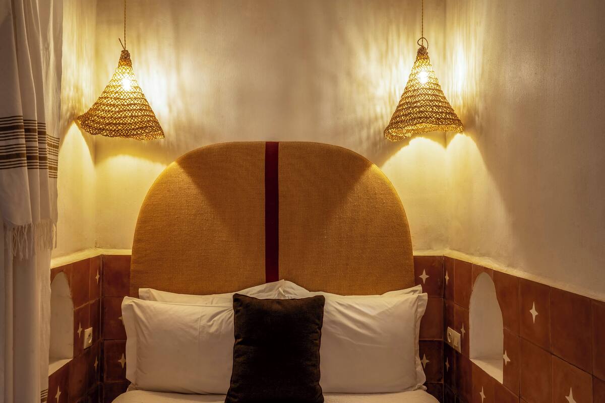 Una cama con cabecera, dos lámparas colgantes y paneles en la pared con diseño de estrellas.