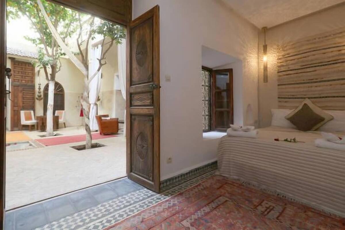 Un dormitorio con cama, un tapete estampado, una puerta de madera y vistas al exterior.