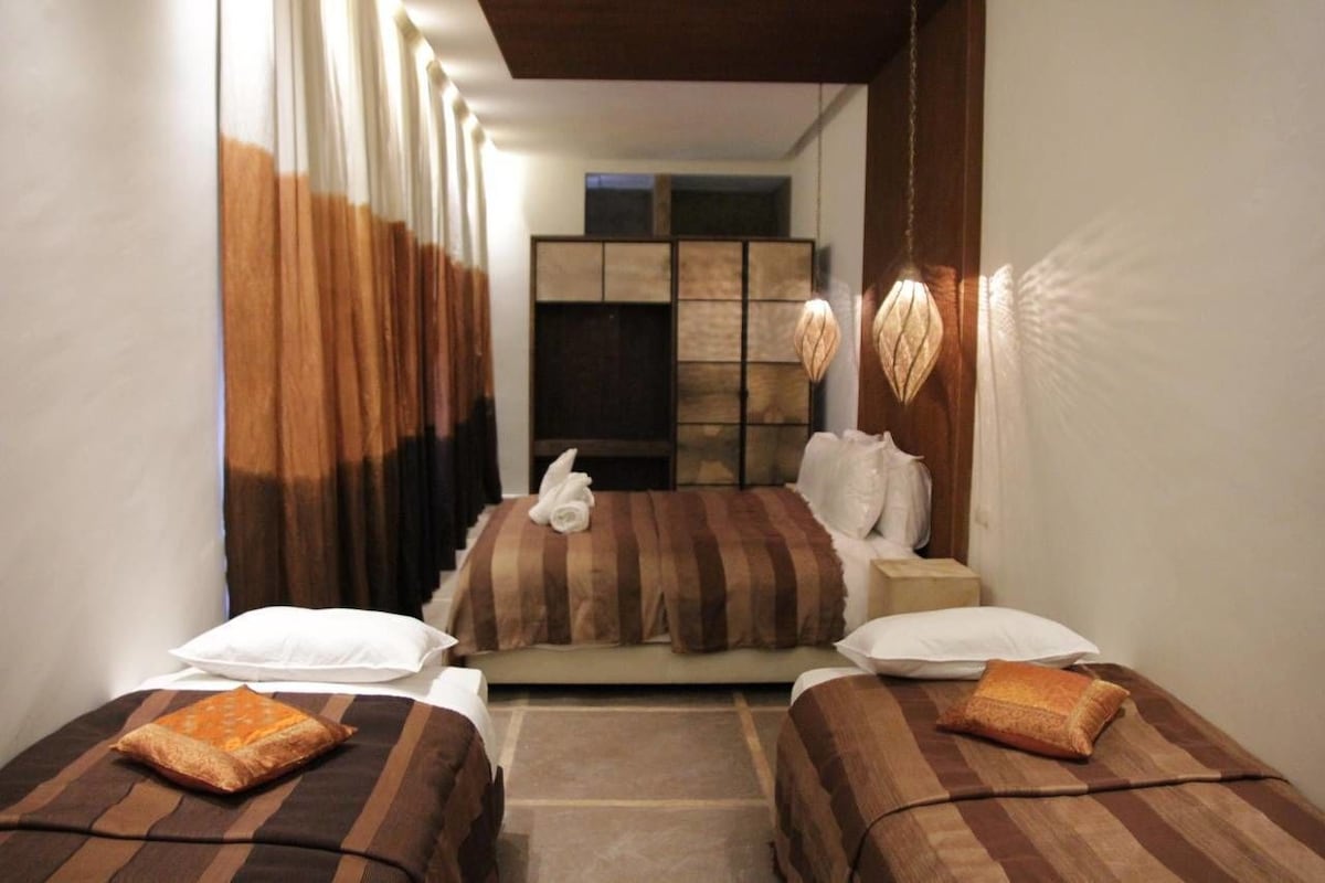 A hotel room with a bed, two bedside tables, a nightstand, a mirror, and a curtain.