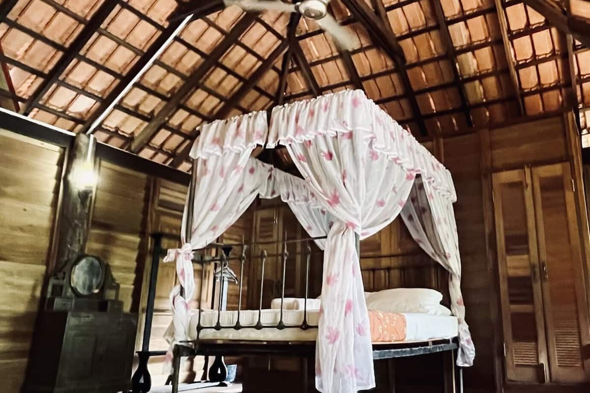 A room with a four-poster bed, a ceiling fan, and wooden walls.