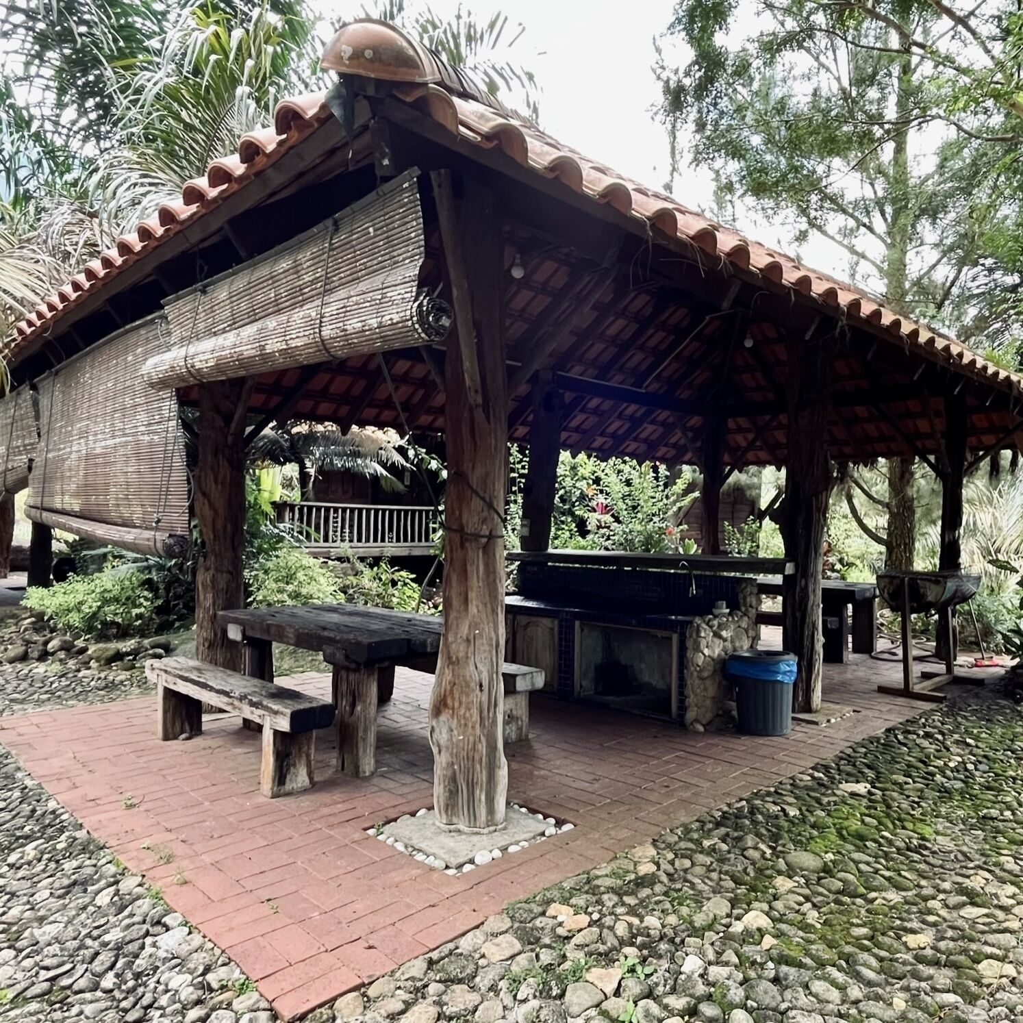 Un pavillon rustique en plein air, doté d’un toit en tuiles, de bancs en bois et d’une cheminée en pierre.