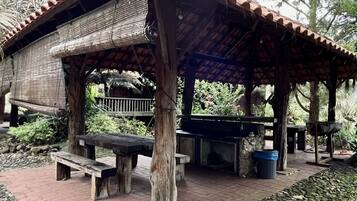 Un pavillon rustique en plein air, doté d’un toit en tuiles, de bancs en bois et d’une cheminée en pierre.