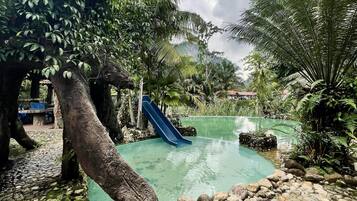 A pool area with a blue slide, surrounded by rocks and lush greenery.