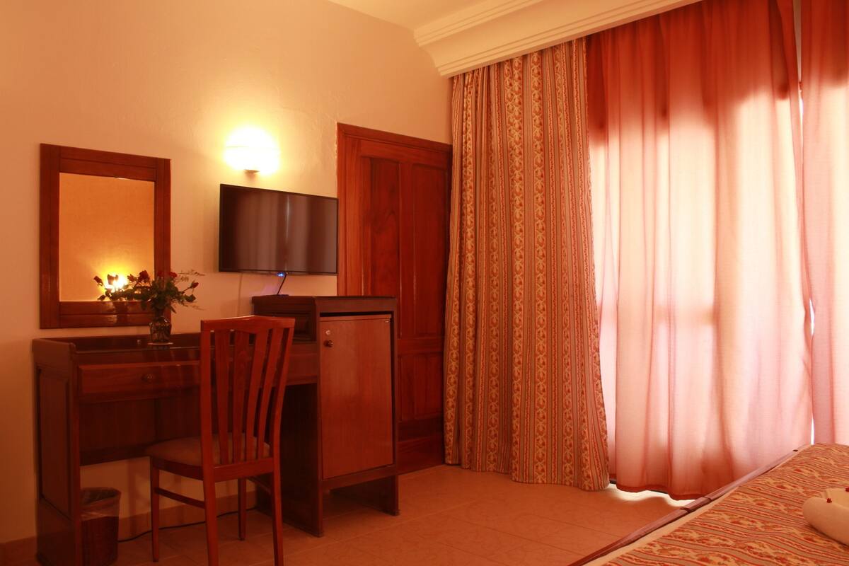 Une chambre d’hôtel avec un bureau en bois, une chaise, une télévision et un lit recouvert d’une courtepointe à motifs.