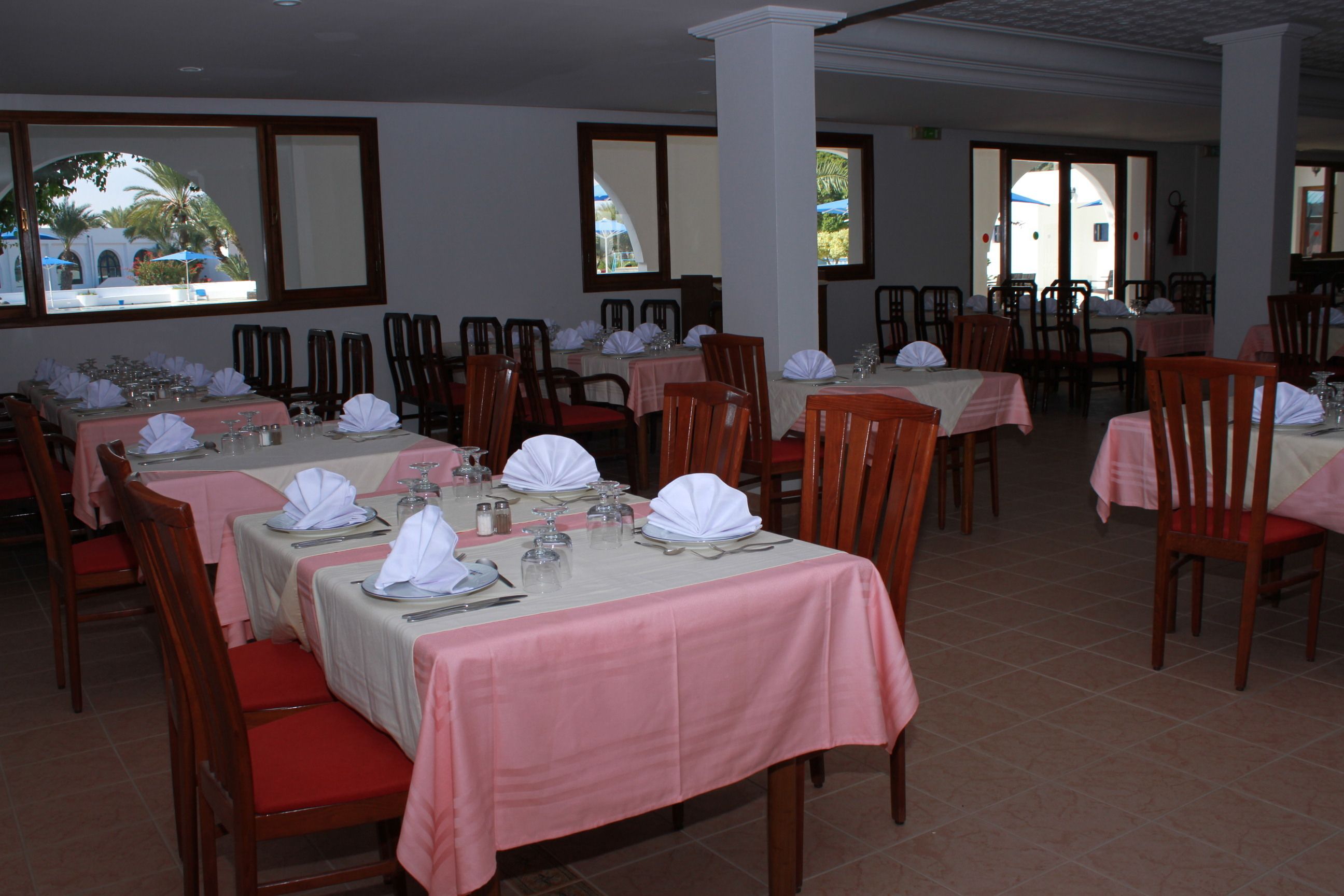 Un restaurante con varias mesas dispuestas para comer, cada una con manteles blancos y sillas rojas.