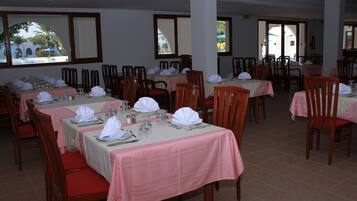Un restaurante con varias mesas dispuestas para comer, cada una con manteles blancos y sillas rojas.