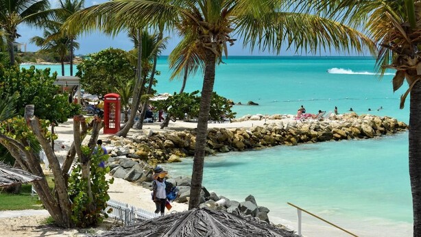 Een strand met palmbomen, een rode telefooncel en een rotsachtige kustlijn.