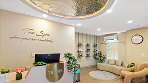 Zona de recepción de un spa con diseño moderno, que incluye un mostrador, un sofá y un estante empotrado con productos de spa.