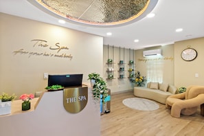 Zona de recepción de un spa con diseño moderno, que incluye un mostrador, un sofá y un estante empotrado con productos de spa.