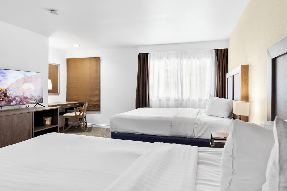 Habitación de hotel con dos camas, un escritorio con silla, televisor y un amplio ventanal con cortinas.