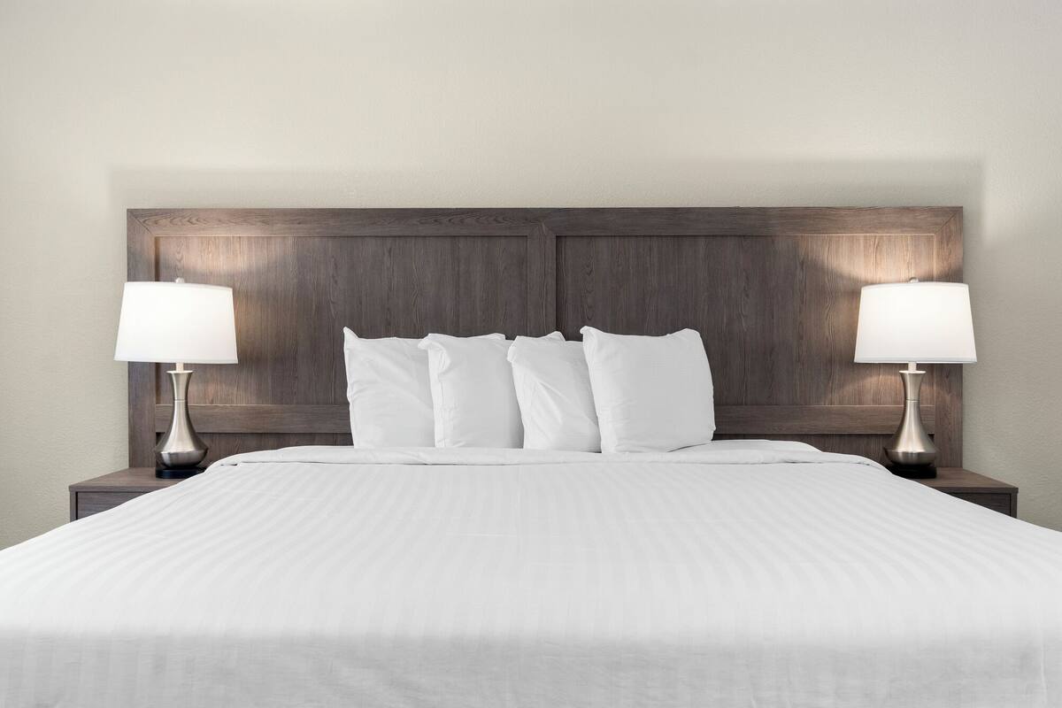 Una cama bien hecha con sábanas blancas, cabecera de madera y dos lámparas de noche.