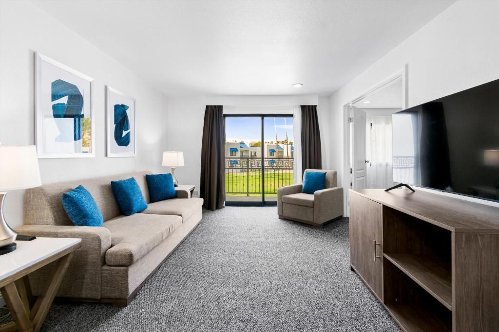 Habitación de hotel con sofá, sillón, televisión y vista a un edificio a través del ventanal.