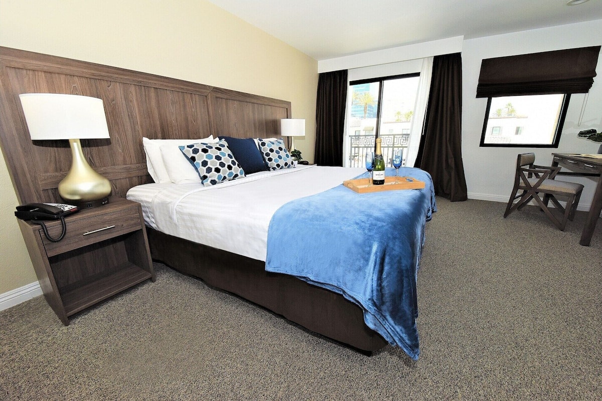 A hotel room with a bed, a desk, a chair, a phone, and a bottle of champagne.