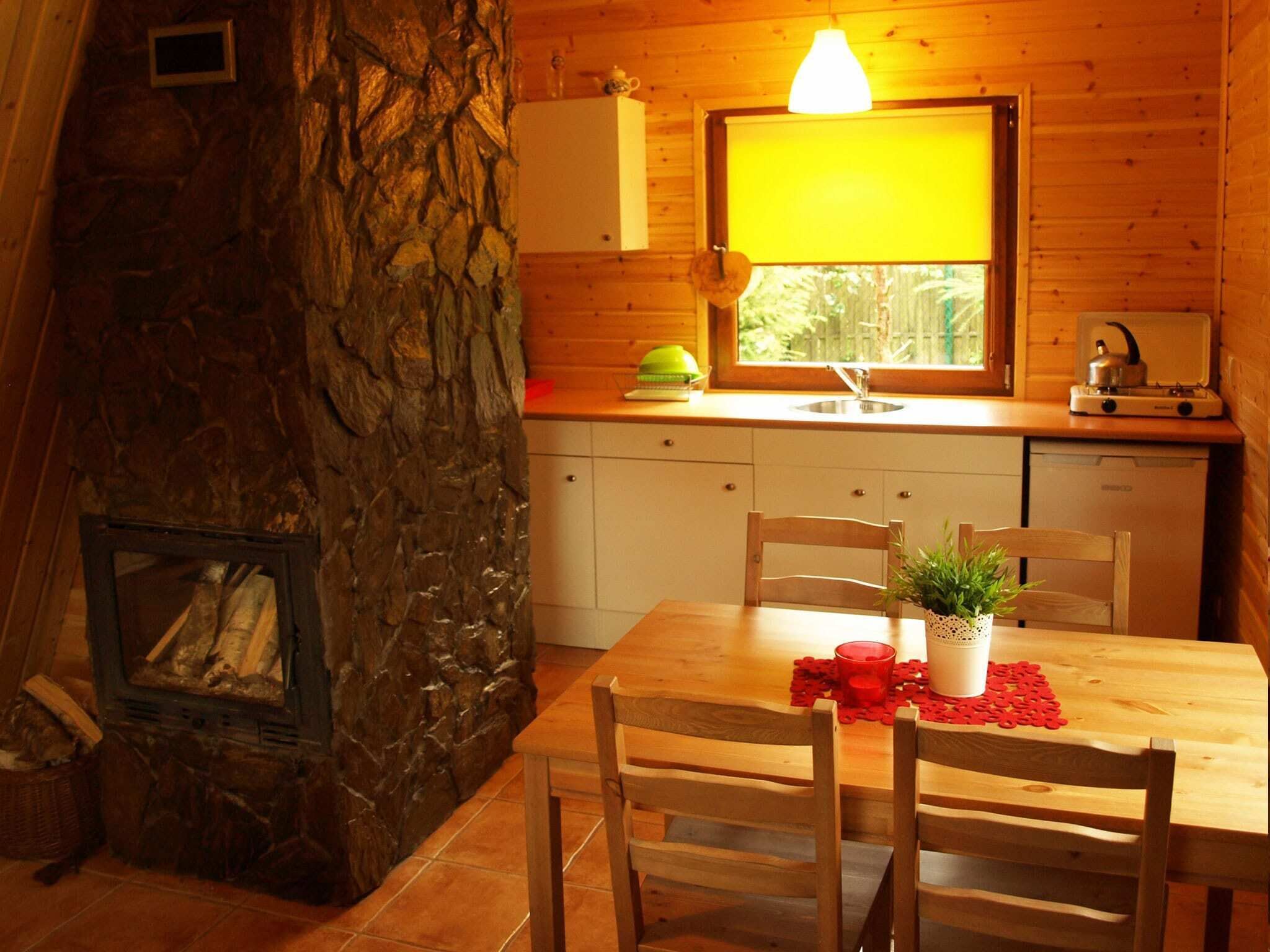 A cozy cabin interior with a stone fireplace, wooden dining table, and a kitchen area with a window.