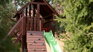Une structure de jeu en bois, dotée d’un toboggan et d’un mur d’escalade, entourée d’arbres.