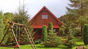 Une grange rustique avec un toit rouge, entourée d’une végétation luxuriante et agrémentée d’une balançoire en bois.