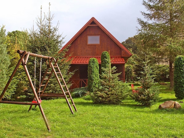 A rustic barn with a red roof, surrounded by lush greenery and a wooden swing set.
