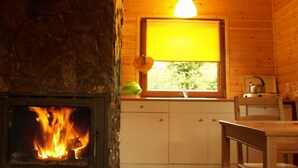 Un intérieur de chalet chaleureux avec une cheminée en pierre, des murs en bois, une fenêtre offrant une belle vue et un petit coin cuisine.