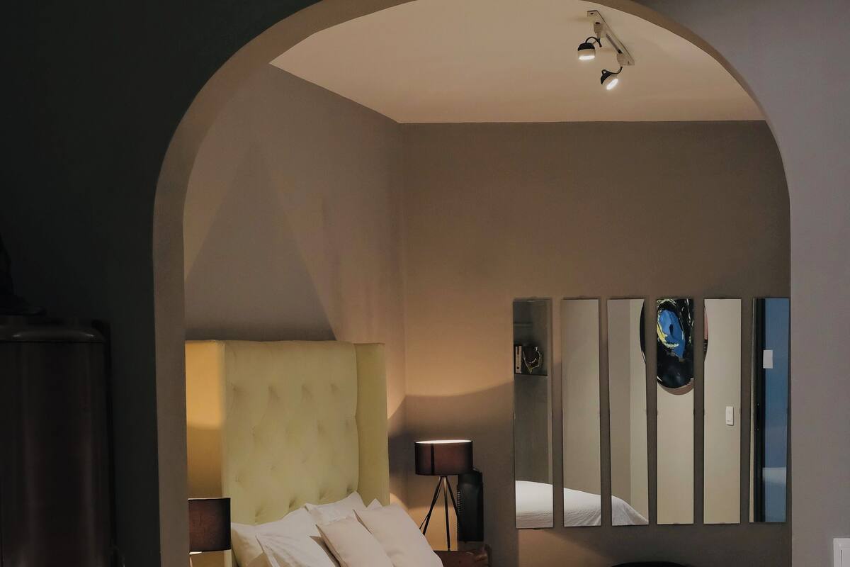 Un dormitorio con una cama, una mesita de noche, una lámpara, un espejo y un armario.
