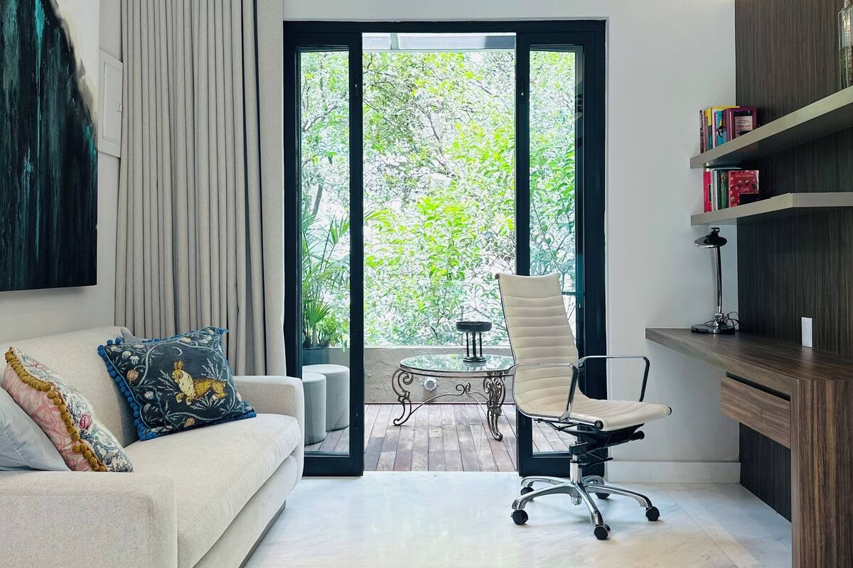 Una sala de estar moderna con un sofá, una mesa de centro y una silla. Hay una estantería y una planta en maceta.