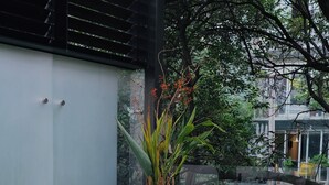 Un área de estar exterior moderna con una mesa de vidrio, sillas con cojines y una pequeña estatua.