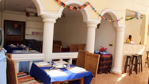 Comedor con mesas dispuestas para una comida, columnas blancas y una persona al fondo.