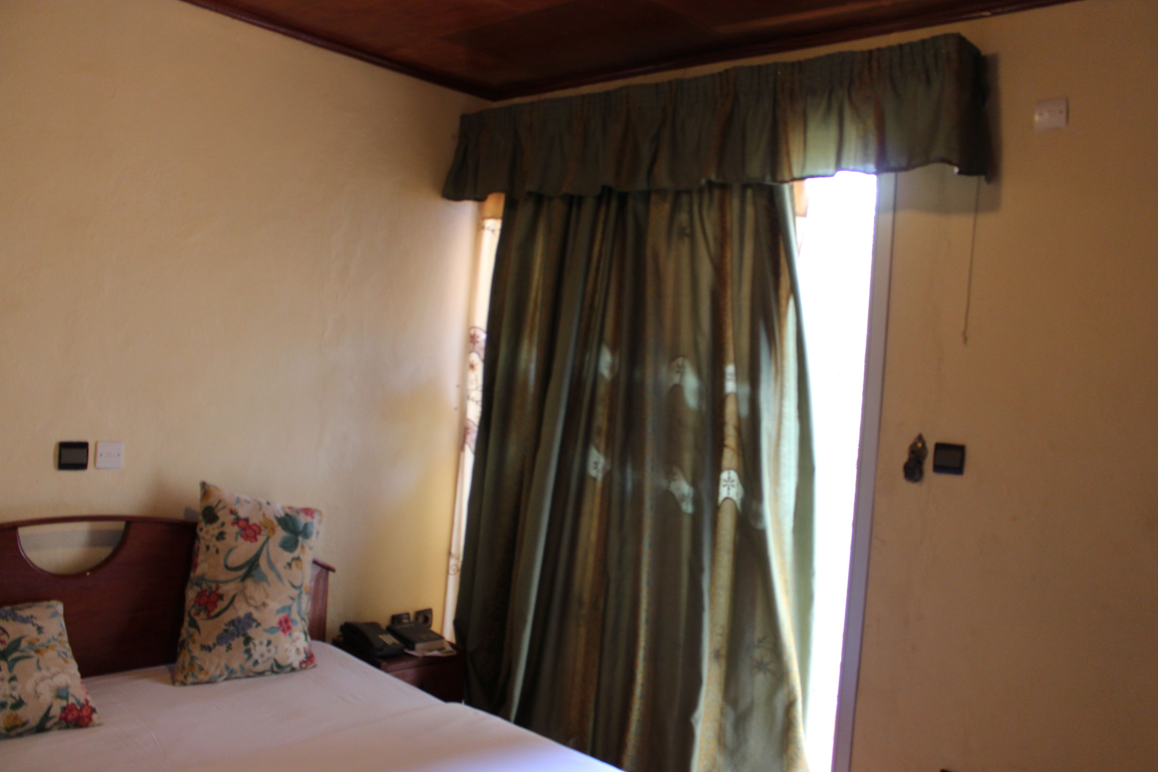 Un dormitorio con cama, almohadas florales, cabecero de madera, mesita de noche y ventana con cortinas.