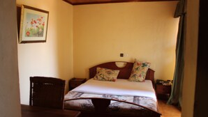 Un dormitorio con una cama de madera, almohadas estampadas, una mesita de noche y una silla de mimbre.