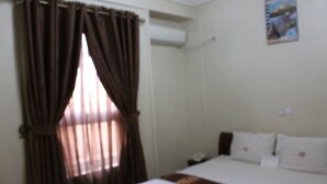 Habitación de hotel con cama, cortinas, aire acondicionado de pared y un cartel en la pared.