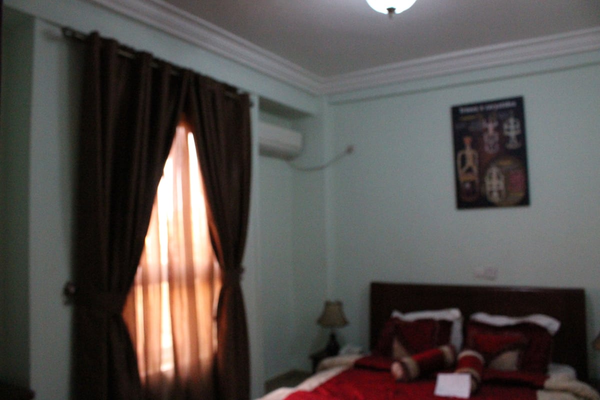 Quarto com cama, cortinas, pôster na parede e mesa de cabeceira com abajur.