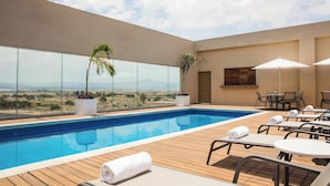 A rooftop infinity pool with wooden decking, lounge chairs, and umbrellas. - Fiesta Inn Silao Puerto Interior (Silao)