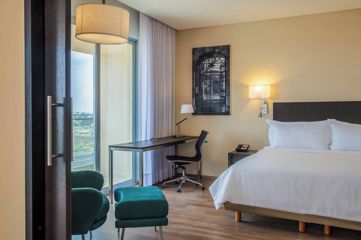 A hotel room with a bed, desk, chair, and a view of the outdoors.