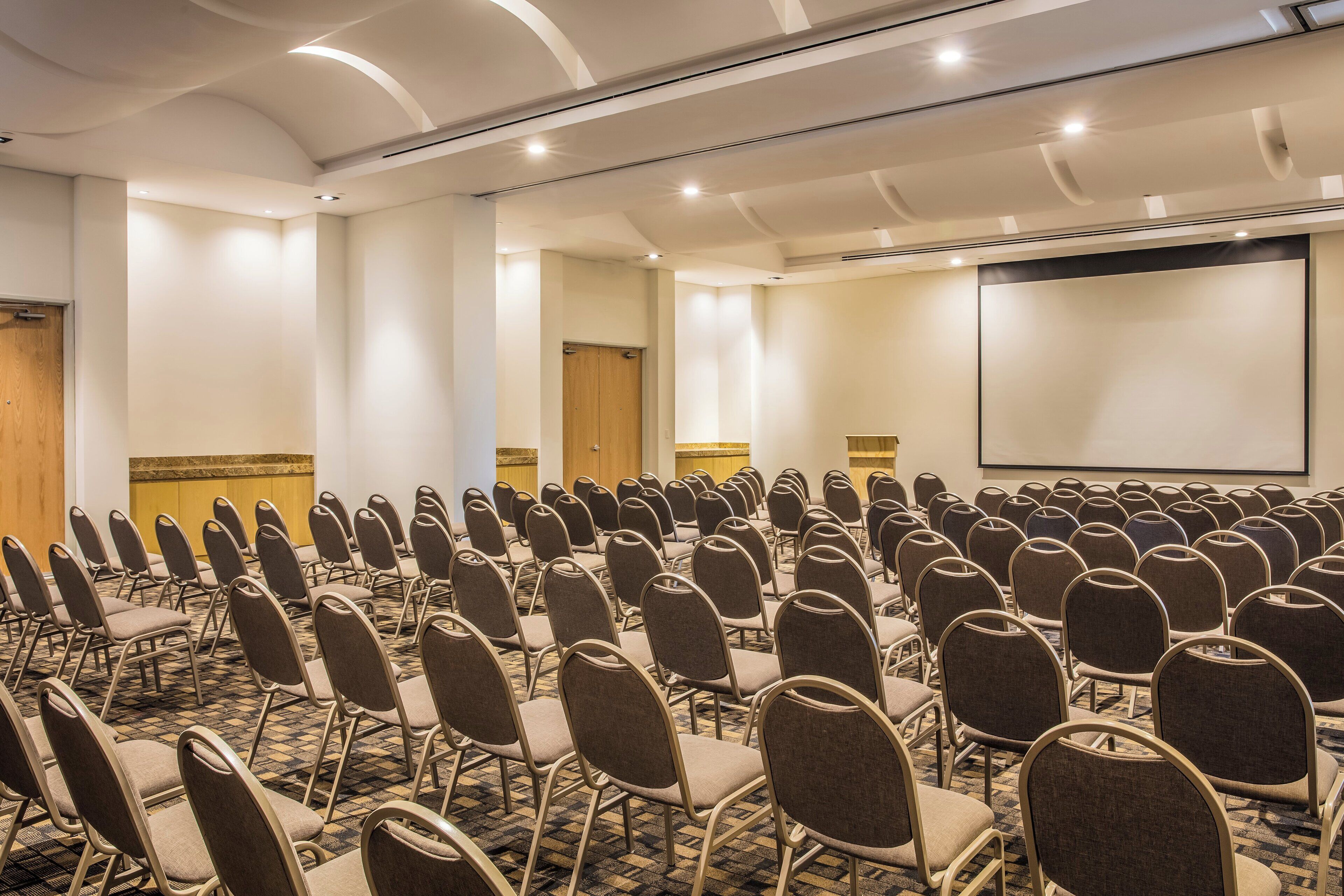 A conference room with rows of chairs, a projector screen, and a carpeted floor.