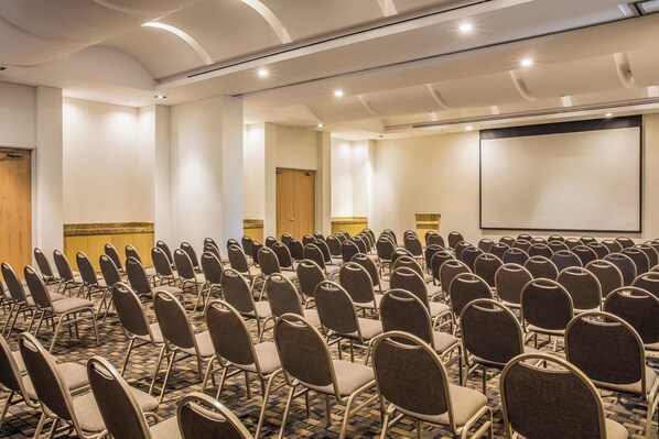 A conference room with rows of chairs, a projector screen, and a carpeted floor.