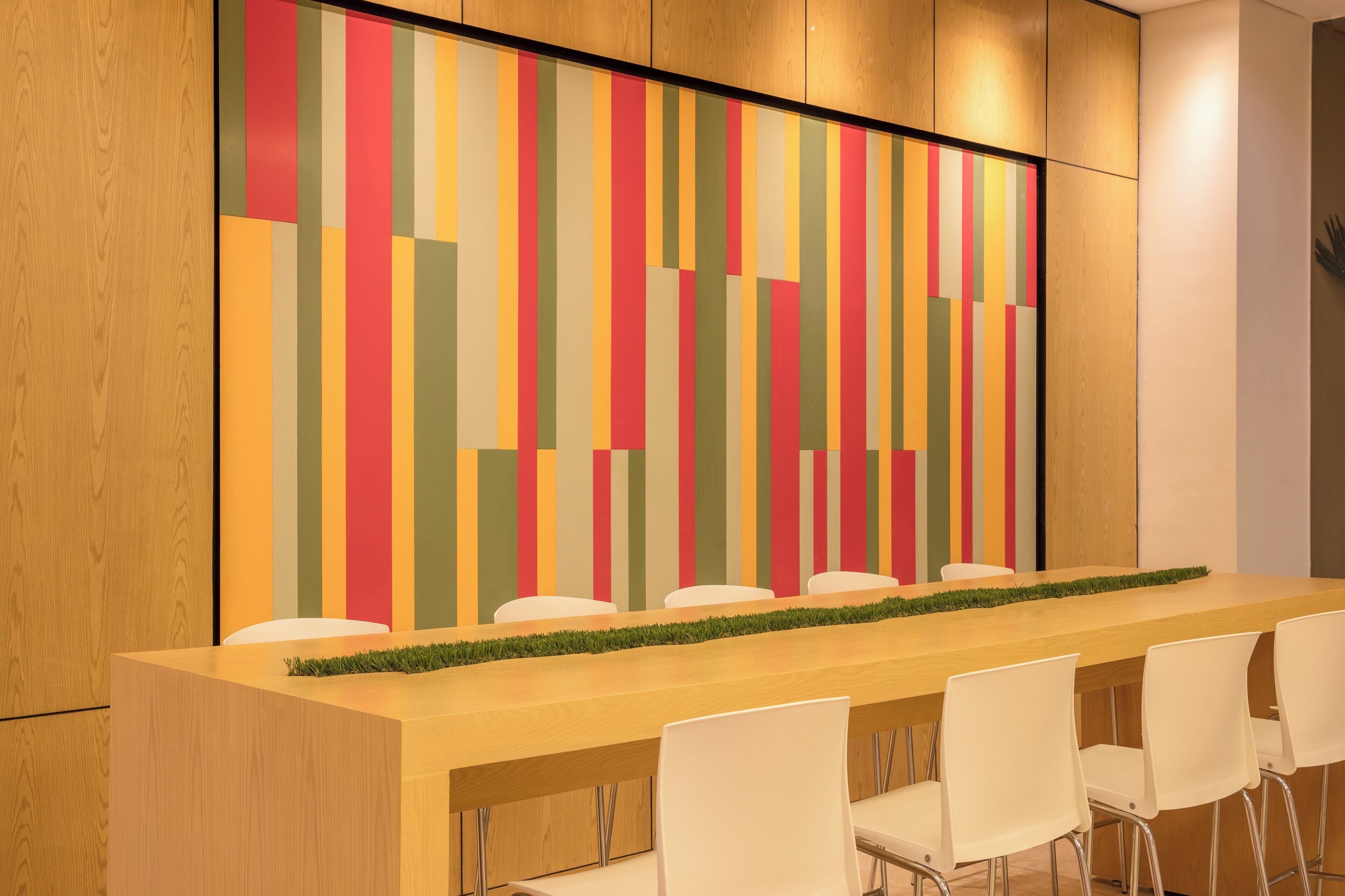 Une salle de conférence avec une longue table en bois, des chaises blanches et un mur rayé aux couleurs vives.