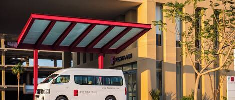 A white van parked in front of a building with a red awning and a sign that reads 'Fiesta Inn.'