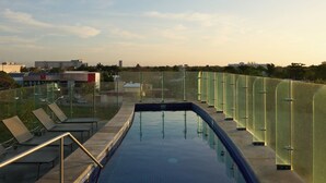 A swimming pool with glass railings, a metal ladder, and lounge chairs.