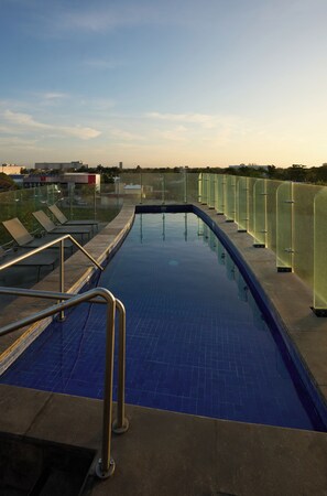 A swimming pool with glass railings, a metal ladder, and lounge chairs.