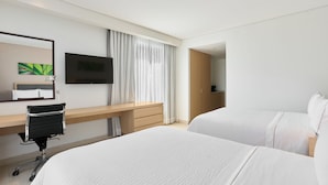 A hotel room with two beds, a desk, a chair, a TV, and a large window with curtains.