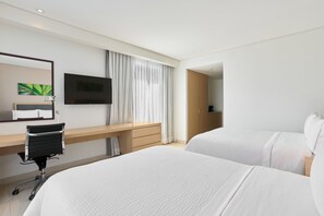 A hotel room with two beds, a desk, a chair, a TV, and a large window with curtains.