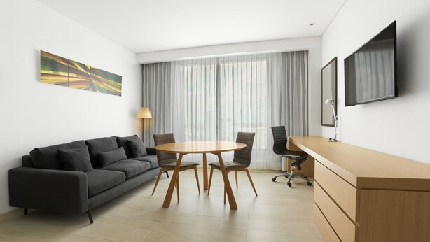A modern room with a sofa, a round table, a desk, and a TV mounted on the wall.