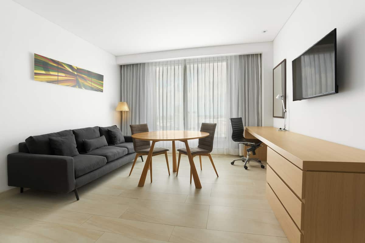 Una habitación moderna con sofá, una mesa redonda, un escritorio y televisor montado en la pared.