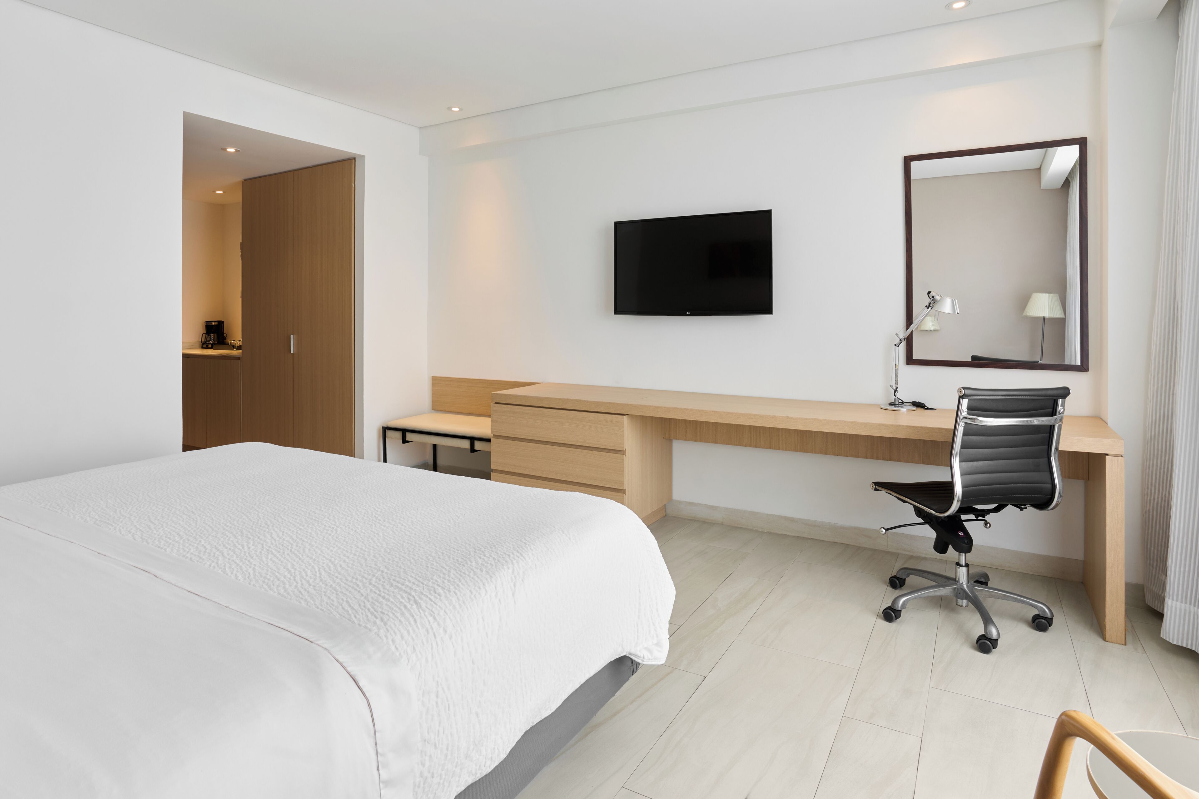 Una habitación de hotel con cama, escritorio, silla, televisión y espejo.