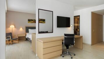 A modern hotel room with a bed, desk, chair, TV, and artwork on the wall.