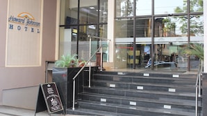 The exterior of Howard Johnson Hotel with a staircase leading to the entrance, a signboard with the hotel's name, and a menu stand outside.