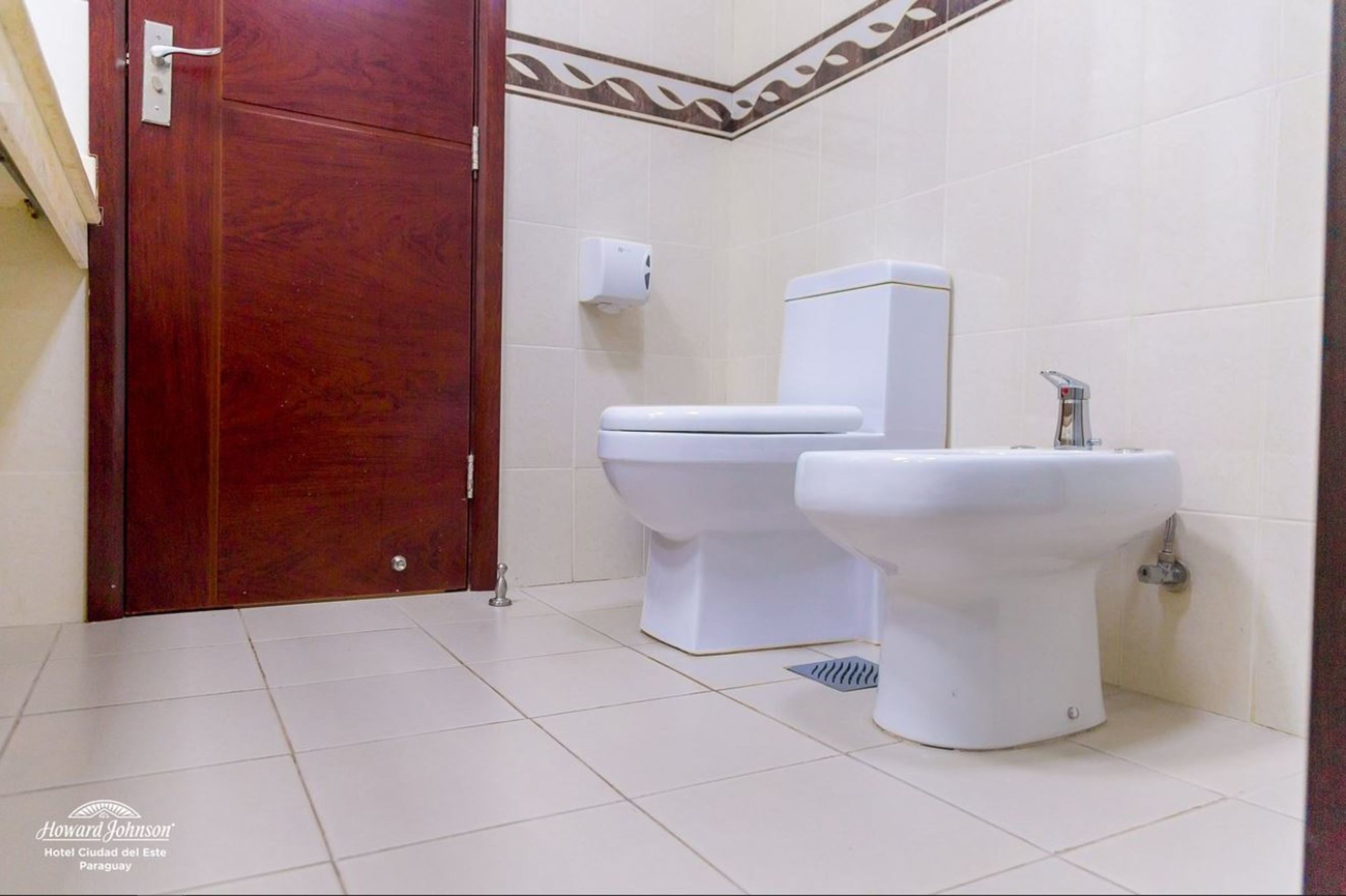 A bathroom with a wooden door, two toilets, a bidet, and a hand dryer.