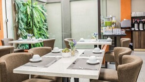 A modern dining area with tables set for service, chairs, and a large green plant in the background.