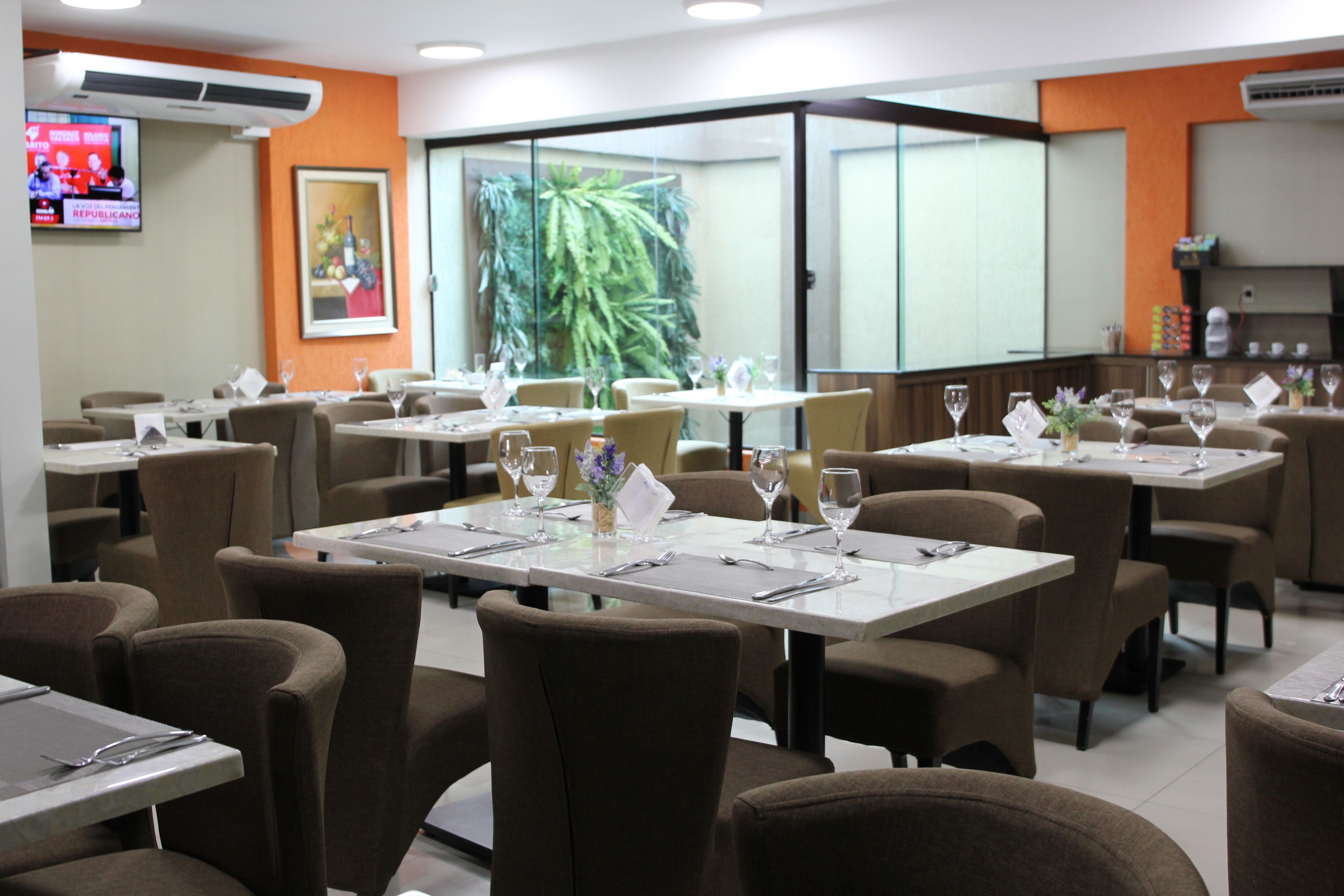 Un restaurant avec plusieurs tables dressées pour le service, des chaises et une grande fenêtre donnant sur un paysage verdoyant.