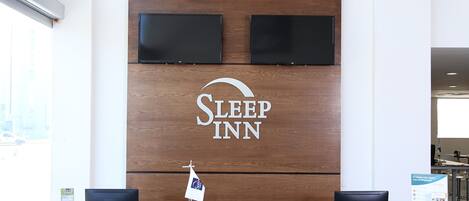 Un mostrador de recepción con un panel de madera, una pantalla de televisión, una bandera y un letrero de Sleep Inn.